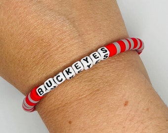 May include: A red and white beaded bracelet with the word "BUCKEYES" spelled out in black letters on white beads.