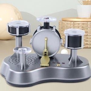 Puede incluir: Un juego de batería de juguete plateado con tambores negros y platillos transparentes. El juego incluye un bombo con pedal, dos tom-toms y una caja. La base es plateada con pequeños orificios para altavoces.