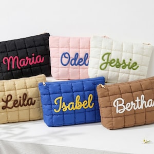 May include: Six quilted cosmetic bags in various colors: black, pink, white, tan, blue, and brown. Each bag features a different name embroidered in a contrasting color: Maria, Odel, Jessie, Leila, Isabel, and Bertha.