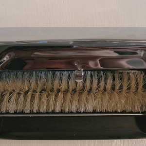May include: A vintage, black and chrome dustpan with a brush. The brush is made of light brown bristles. The chrome lid is open, revealing the brush. The dustpan is rectangular.