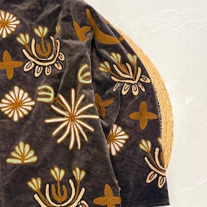 Puede incluir: Una chaqueta de terciopelo gris oscuro con bordados intrincados en tonos amarillo mostaza, crema y verde menta claro. El dise&ntilde;o consiste en varios motivos florales y en forma de estrella repartidos por la parte delantera y la manga larga.