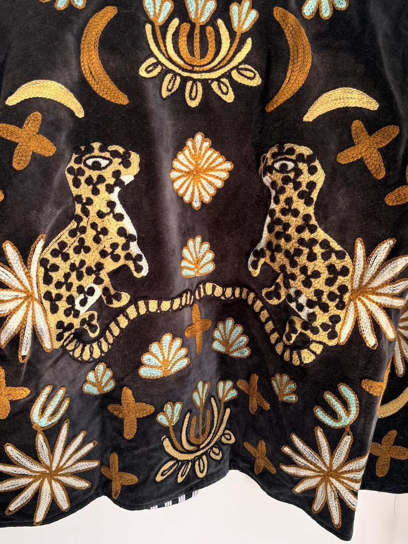 Puede incluir: Un tejido de terciopelo gris oscuro con un intrincado bordado de dos leopardos moteados frente a frente. El dise&ntilde;o incluye motivos florales, lunas crecientes y formas de cruz en amarillo dorado y azul claro dispuestos sim&eacute;tricamente.