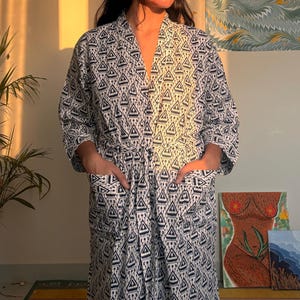 Könnte beinhalten: Weißes und marineblaues Muster-Kimono mit geometrischem Design. Der Kimono hat einen Bindegürtel, Taschen und lange Ärmel. Der Kimono ist aus leichtem Stoff gefertigt.