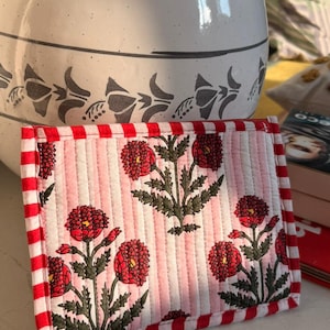 Könnte beinhalten: Ein rechteckiger, gesteppter Untersetzer mit floralem Muster. Er hat einen rot-weiß karierten Rand und einen rosa-weiß gestreiften Hintergrund. Rote Blumen mit grünen Blättern sind auf dem Untersetzer abgebildet.