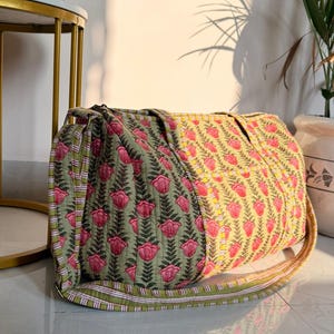 Può includere: Una borsa da viaggio trapuntata con motivo floreale. La borsa presenta pannelli verde oliva e gialli, ciascuno decorato con un motivo ripetuto di fiori rosa e foglie verdi. Ha una tracolla abbinata.