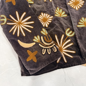 Puede incluir: Una chaqueta de terciopelo gris oscuro con bordados intrincados en tonos amarillo mostaza, blanco y verde menta claro. El dise&ntilde;o incluye varios motivos de estrellas, flores y formas de media luna sobre la tela.