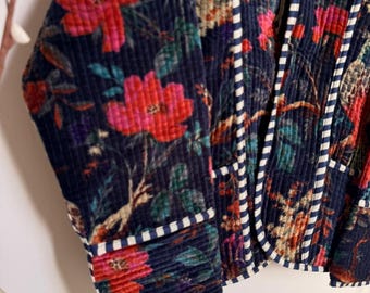 May include: A navy blue corduroy jacket with a vibrant floral pattern in red, pink, and green. The jacket features white and navy striped trim along the edges and pockets, creating a striking contrast.