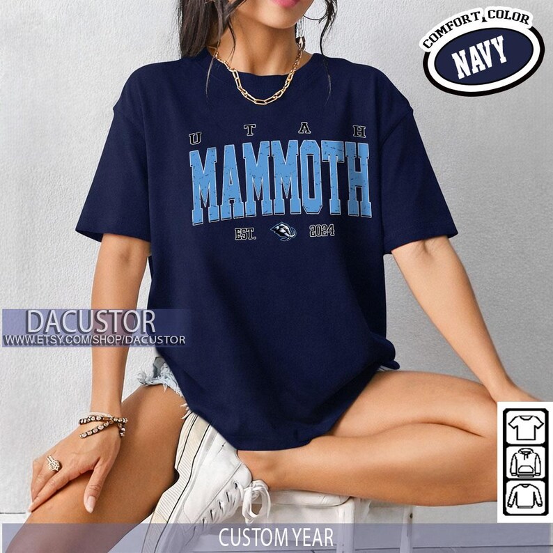 May include: Navy blue t-shirt featuring "UTAH MAMMOTH" in light blue lettering. The shirt includes "EST. 2024" and a logo. The words "COMFORT, COLOR NAVY" are printed on the top right. The Etsy shop name "DACUSTOR" is printed on the bottom left.