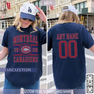 Op de afbeelding: Marineblauw t-shirt met "MONTREAL CANADIENS" in rode letters en een logo. De achterkant heeft "ANY NAME" en het nummer "00" in rood. Het shirt is aanpasbaar met een aangepast jaar, nummer en naam.