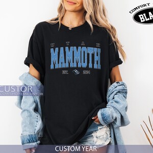 May include: Black t-shirt featuring the words "UTAH MAMMOTH" in light blue, with "EST. 2024" below. The shirt has a distressed, vintage appearance. The words "COMFORT COLOR BLACK" are printed on the top right.