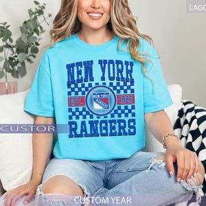 May include: Lagoon blue t-shirt featuring the text "NEW YORK RANGERS" with a team logo and "EST. 1926". The shirt has a checkered pattern and is a custom year design.