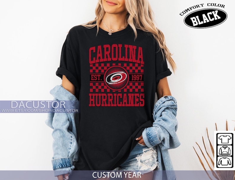 May include: Black t-shirt with a red and white graphic design. The design features the text "CAROLINA HURRICANES" with the team logo and "EST. 1997". The shirt is labeled "COMFORT COLOR BLACK" and "CUSTOM YEAR".