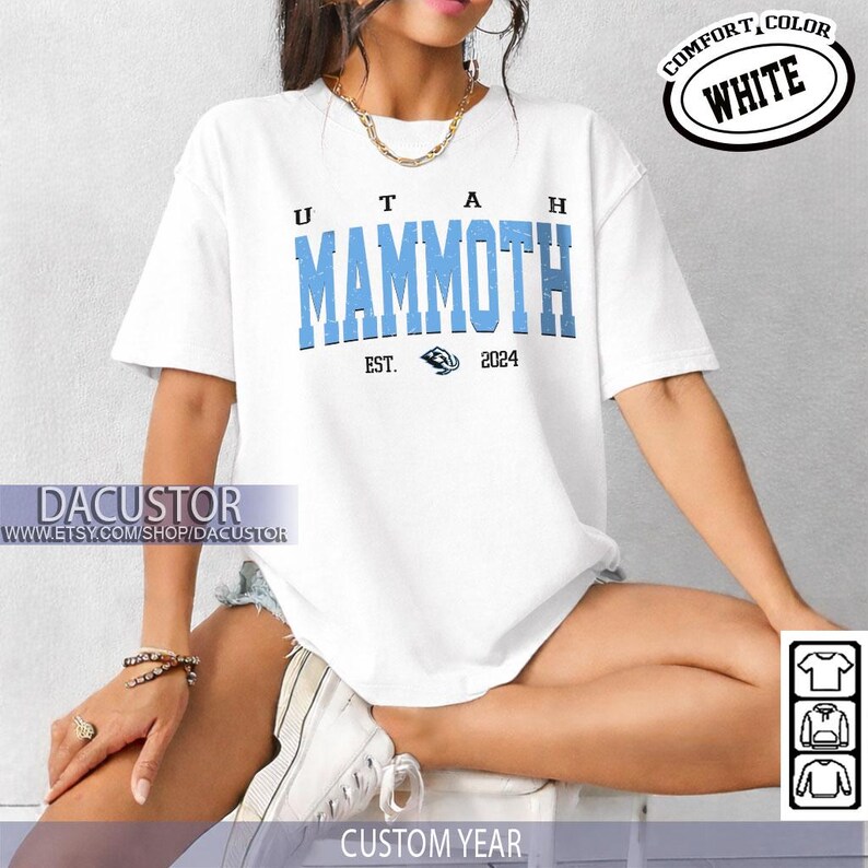 May include: White t-shirt with the text "UTAH MAMMOTH" in light blue block letters. The shirt also features the text "EST. 2024" and a Mammoth logo. The words "COMFORT, COLOR WHITE" are in a circle on the top right.