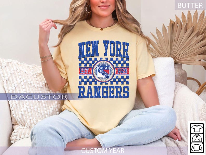 May include: A light yellow t-shirt featuring the text "NEW YORK RANGERS" in blue block letters. The shirt includes a circular logo with the team name and "EST. 1926". The shirt is a comfortable fit.
