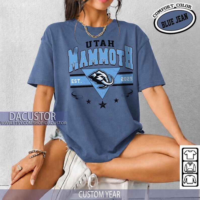 K&ouml;nnte beinhalten: Blaues Jeans-T-Shirt mit dem Schriftzug "Utah Mammoth" in Hellblau und einer stilisierten Elefanten-Grafik. Das Shirt enth&auml;lt den Text "EST. 2025" und die Worte "Comfort Color" in einem kreisf&ouml;rmigen Design. Der Etsy-Shop-Name "Dacustor" ist ebenfalls sichtbar.