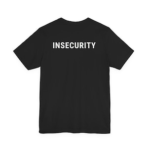 Op de afbeelding: Een zwart T-shirt met korte mouwen en het woord INSECURITY in dikke, witte hoofdletters op de bovenkant van de borst. Het kledingstuk heeft een standaard ronde hals en een rechte zoom, wat zorgt voor een eenvoudig en strak ontwerp.