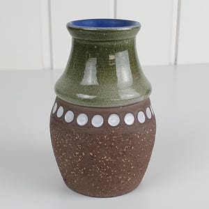 Könnte beinhalten: Eine Keramikvase mit einem glatten, glänzend olivgrünen Oberteil und einem strukturierten, gesprenkelten braunen Unterteil. Ein horizontales Band aus kleinen, erhabenen weißen Punkten umkreist die Mitte, und der Innenrand ist kobaltblau.