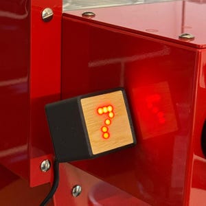 Puede incluir: Primer plano de una máquina de espresso roja con una pantalla digital que muestra el número 7 en rojo. La pantalla está alojada en una caja rectangular negra y de madera. Un medidor es visible en la parte inferior.