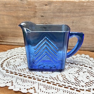 May include: A blue glass pitcher with a geometric design. The pitcher has a square body and a handle.