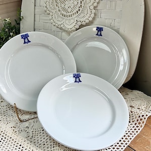 May include: Three white ceramic plates with blue trim and a bell design. The plates are stacked on top of each other.