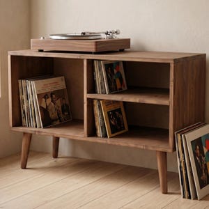 May include: A wooden record player stand with a turntable on top. The stand has open shelving filled with vinyl records and CDs. The wood has a warm, natural finish, and the stand has angled legs.