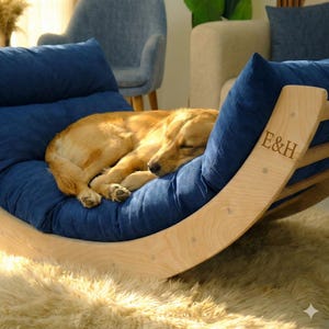A golden retriever dog is curled up and sleeping on a blue cushion with the letters "E&H" carved into it.