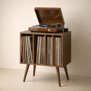 Może przedstawiać: Drewniany gramofon z wykończeniem z orzecha włoskiego stoi na pasującej szafce. Szafka ma przegrody wypełnione płytami winylowymi i jest wspierana przez skośne nogi. Gramofon ma otwartą pokrywę, odsłaniającą gramofon i niebieską płytę.