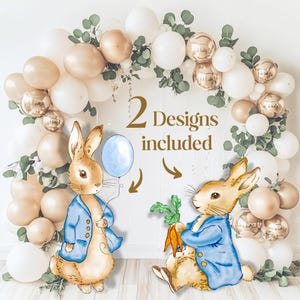 May include: Two watercolour-style rabbit illustrations wearing blue jackets, one holding a light blue balloon and the other holding orange carrots, set against a balloon arch of white, beige, and metallic gold balloons with green eucalyptus leaves.