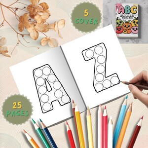 May include: An open alphabet colouring book with the letters "A" and "Z" outlined with circles. The book is open to two pages, with a hand holding a pencil. The cover reads "ABC Alphabet Colouring Book". Colouring pencils are scattered around the book. The cover says "5 COVER" and "25 PAGES".