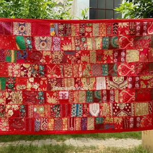 Puede incluir: Textil de retazos rojo rectangular con una variedad de patrones y texturas. El patchwork incluye diseños florales y geométricos en tonos de rojo, dorado y verde. El textil tiene un borde rojo liso. El texto "ShivaayFashion" es visible.
