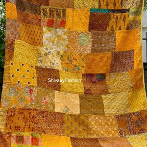 Könnte beinhalten: Ein Patchwork-Quilt in Gelb- und Brauntönen, bestehend aus rechteckigen Stoffflicken. Der Quilt weist verschiedene Muster und Texturen auf. Der Quilt wird von zwei Händen gehalten, mit dem Text "ShivaayFashion" sichtbar.