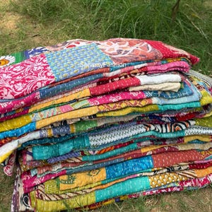 May include: A stack of colorful, patchwork quilts. The quilts feature a variety of patterns and colors, including pink, blue, yellow, and red. The quilts are made of a soft, quilted material and appear to be handmade. The text "ShivayFashion" is visible on the quilts.
