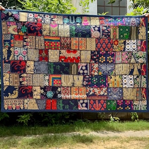 May include: A rectangular patchwork quilt with a dark blue border. The quilt is composed of numerous fabric squares in various colors, including red, gold, green, and blue. The squares feature intricate patterns and designs. The text "Shivaayfashion" is visible.