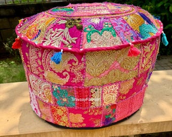 May include: A round patchwork pouf in pink, gold, and multi-coloured fabrics. The pouf features intricate embroidery and decorative tassels. The text "ShivaayFashion" is visible on the side. This decorative piece adds a bohemian flair to any space.