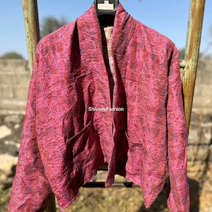 Könnte beinhalten: Eine magentafarbene Jacke mit Paisley-Muster und zwei Vordertaschen hängt an einem Metallgestell. Die Jacke hat einen Schalkragen und ein Futter mit Blumenmuster. Der Text "ShivaayFashion" ist sichtbar.