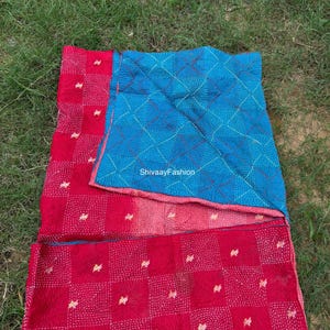 May include: A reversible quilt with a red and blue color scheme. The red side features a grid pattern with white stitching, while the blue side has a diamond pattern. The quilt is lying on green grass.