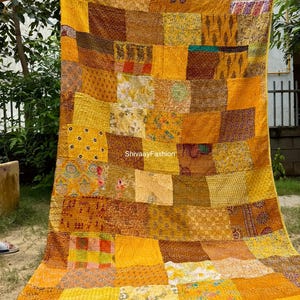 May include: A patchwork quilt with a variety of yellow, gold, and brown fabrics. The quilt is made of rectangular patches with different patterns and textures. The quilt is held up by two hands, and the text "ShivaayFashion" is visible.