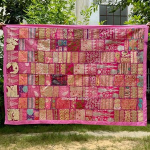 May include: A pink patchwork textile with a variety of patterns and textures. The textile is made up of numerous squares in shades of pink, gold, and other colors. The edges are trimmed with a solid pink border. The text "ShivaayFashion" is visible.