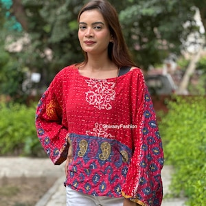 Op de afbeelding: Een rood shirt met lange mouwen, voorzien van een witte bloemenprint op de borst en een blauw paneel bij de taille met gele en blauwe paisley-patronen. Het kledingstuk heeft een wijde halslijn en witte stiksels. De tekst luidt ShivaayFashion.