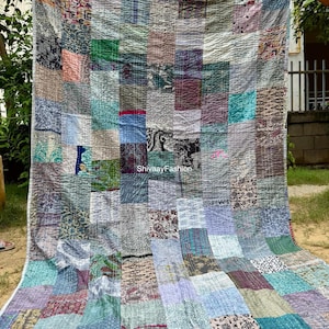 Könnte beinhalten: Eine große Patchwork-Steppdecke mit einer Vielzahl von Stoffmustern und -farben, darunter Blau, Grün und Lila. Die Steppdecke besteht aus rechteckigen Flicken und hat sichtbare Nähte. Das Design ist eine Mischung aus Texturen und Drucken.