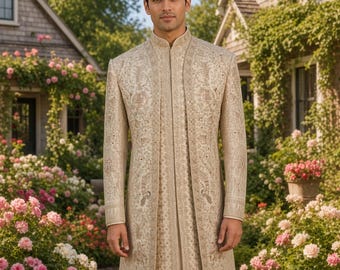 May include: A beige sherwani featuring intricate gold embroidery and sequin detailing, worn over plain off-white trousers. The long-sleeved coat has a high mandarin collar and a structured, open-front design that reaches below the knees.