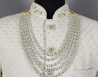 Könnte beinhalten: Elfenbeinfarbene Jacke mit langen Ärmeln, dezentem geometrischen Muster, verzierten Knöpfen und Stehkragen. Eine mehrreihige Perlenkette ist über der Jacke drapiert. Die Jacke wird auf einer Schaufensterpuppe präsentiert.
