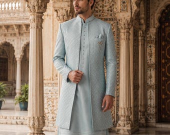 Puede incluir: Un conjunto sherwani azul claro que presenta una chaqueta de manga larga texturizada con cuello mao y bordados intrincados, usado sobre una kurta azul claro lisa a juego y pantalones ajustados, completado con un pañuelo de bolsillo y zapatos claros.