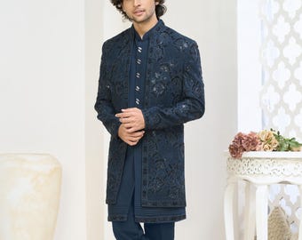 May include: A navy blue embroidered jacket and matching pants. The jacket features intricate floral patterns and is worn over a solid navy blue shirt. The outfit is completed with navy blue pants and dark blue shoes. The ensemble is formal wear.