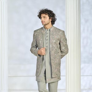 Puede incluir: Un conjunto gris bordado que incluye una chaqueta y un pantal&oacute;n a juego. La chaqueta presenta intrincados patrones florales en rosa y blanco. El conjunto incluye una camisa con cuello mandar&iacute;n, ideal para ocasiones formales.