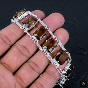 May include: A silver link bracelet featuring a series of rectangular, faceted smoky quartz gemstones. Each stone is held in a prong setting, connected by polished silver links that create a continuous, articulated chain design along the wrist.