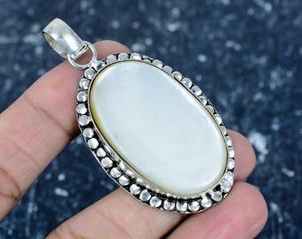Könnte beinhalten: Ovaler Anhänger mit einem perlmuttweißen Mittelstein, umgeben von einem silberfarbenen Metallrahmen mit einem Perlenrand. Der Anhänger hat eine silberne Öse zum Anbringen an einer Kette.