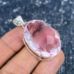Könnte beinhalten: Ein großer, facettierter, ovalförmiger rosa Edelsteinanhänger mit einer silbernen Öse. Der Edelstein hat einen hellrosa Farbton mit inneren Einschlüssen. Der Anhänger ist in einen silbernen Rahmen gefasst.