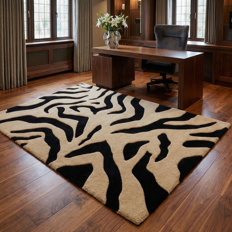 Pu&ograve; includere: Un tappeto rettangolare con un motivo a strisce zebrate in nero e beige. Il tappeto &egrave; posizionato su un pavimento in legno in una stanza con una scrivania, una sedia e finestre.