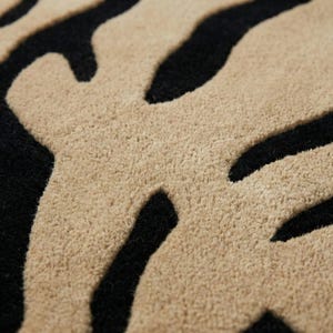 Pu&ograve; includere: Primo piano di un tappeto con motivo zebrato. Il tappeto presenta strisce nere e beige alternate, creando un design audace e strutturato. Le fibre del tappeto appaiono morbide e soffici, adatte all'arredamento della casa.
